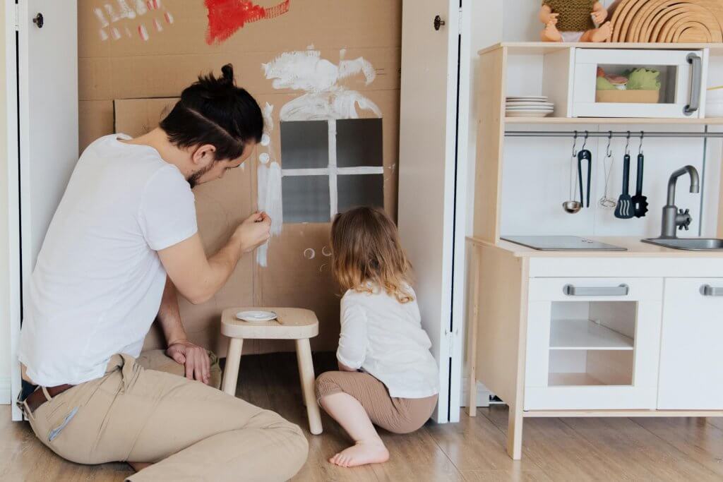 Father and daughter painting a carton wall and creating together a sensory play corner. 